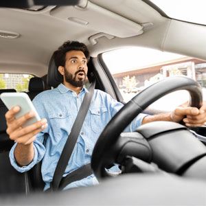 Shocked driver holding a phone while driving, illustrating car accident risk - Pigott Law Group