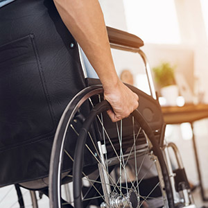A disabled man is sitting in a wheelchair. He holds his hands on the wheel. Nearby are his colleagues