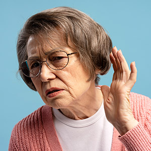 Elderly woman with round glasses holding her hand to her ear, illustrating Vision Or Hearing Loss
